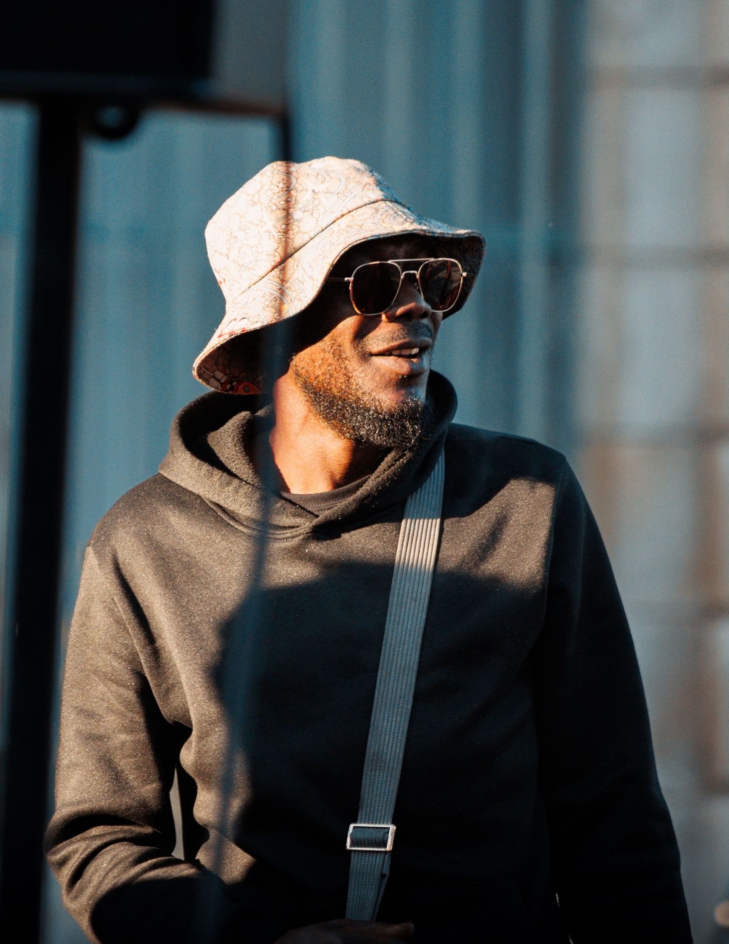 Person in beige bucket hat and hoodie wearing sunglasses in natural lighting.