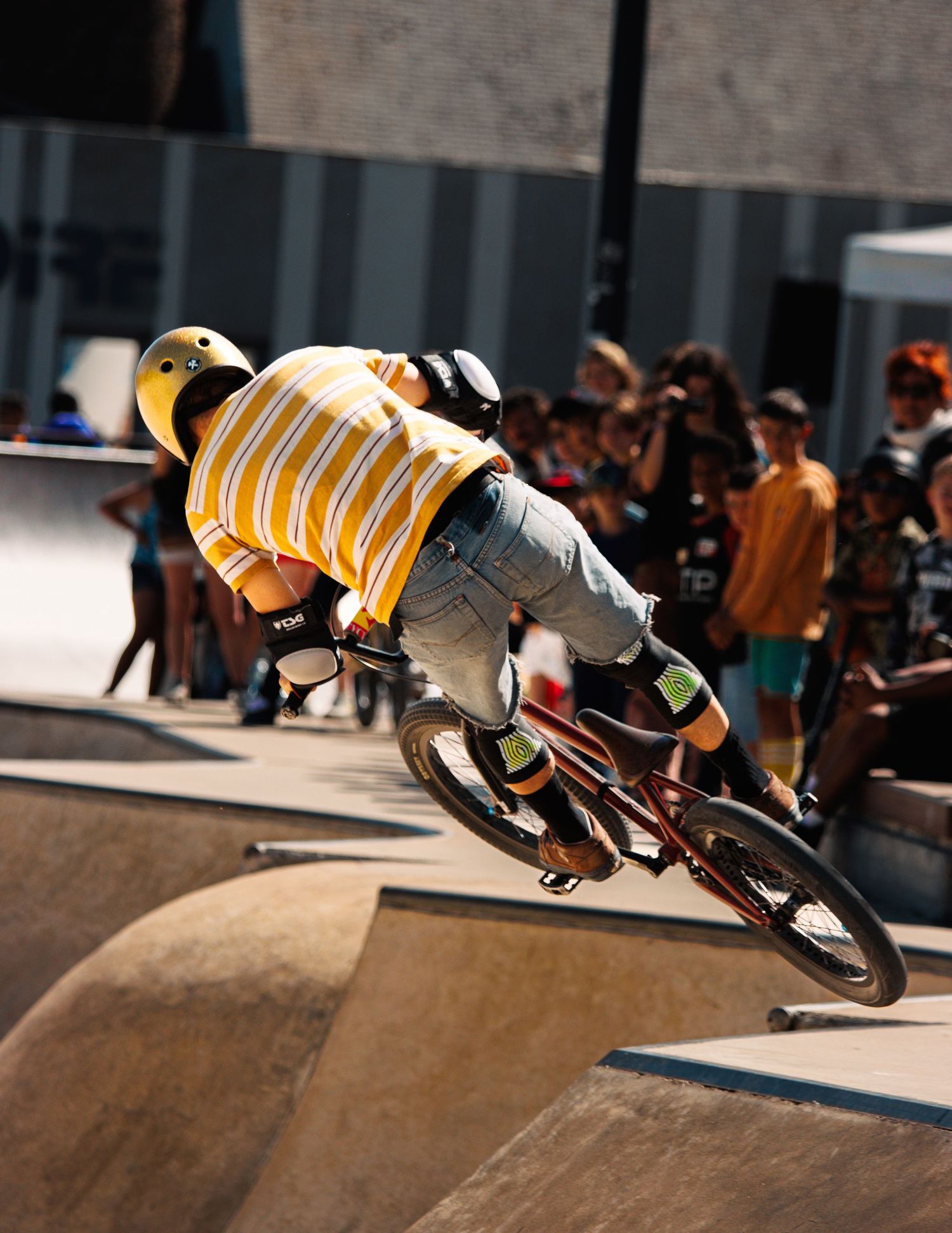 BMX athlete in yellow striped shirt performing aerial stunt at skate competition.