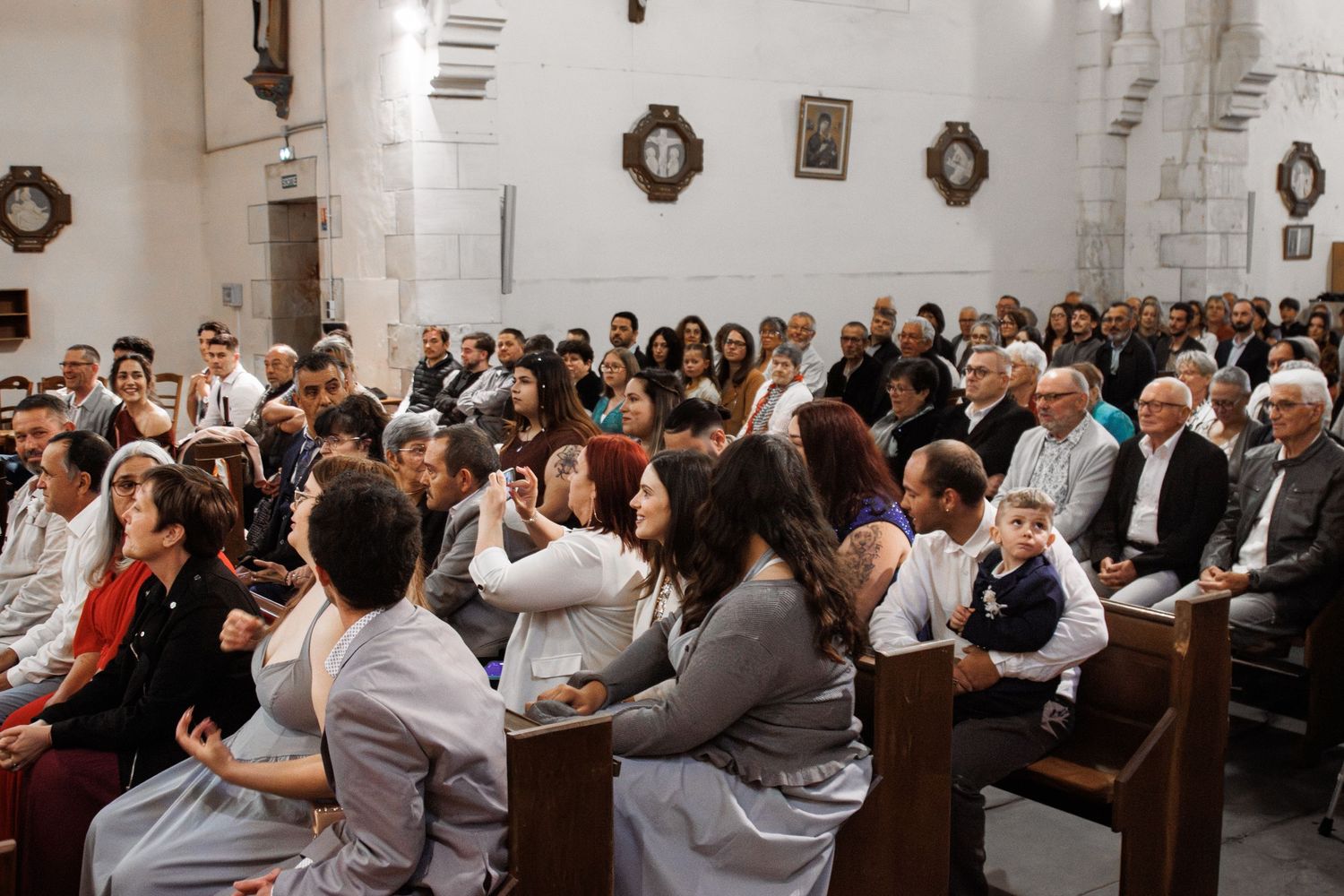 Congregation gathered inside a historic church during a religious ceremony, seated in wooden pews with ornate walls.