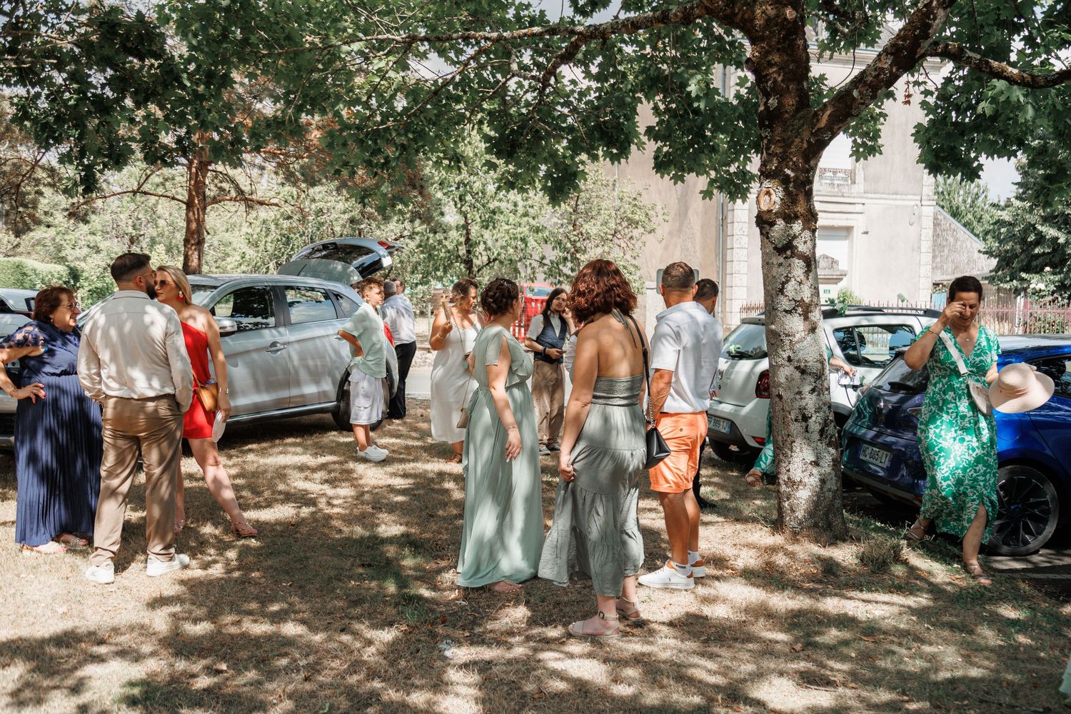 Bridesmaids in sage green dresses gathering outdoors under trees at a wedding celebration.