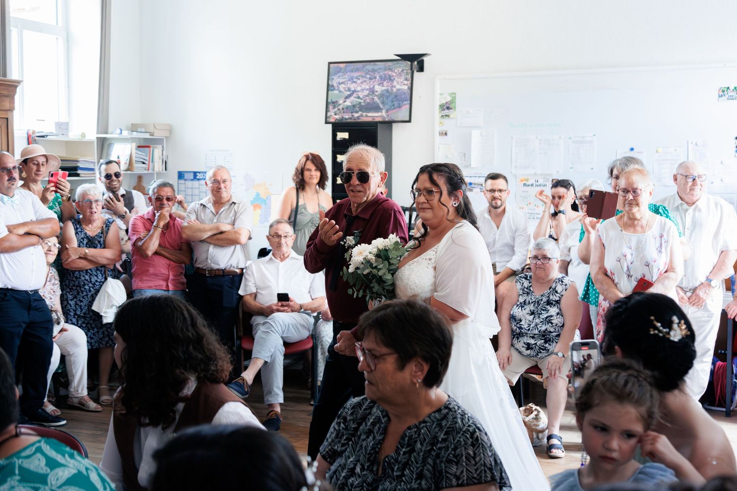 Bride in white dress walking through applauding wedding guests while holding a white floral bouquet.