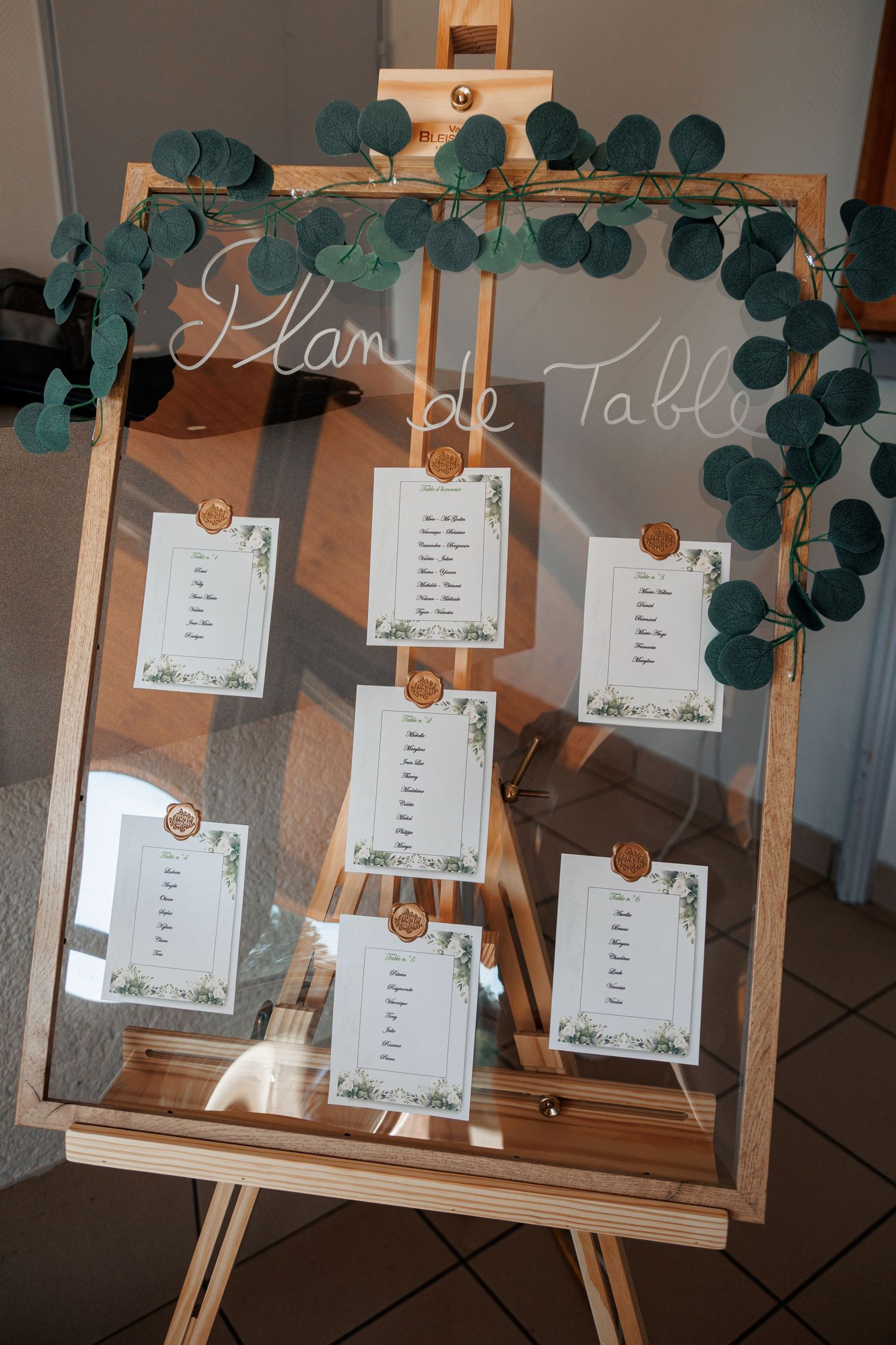 Wooden easel displaying Plan de Table seating chart with eucalyptus botanical decor.