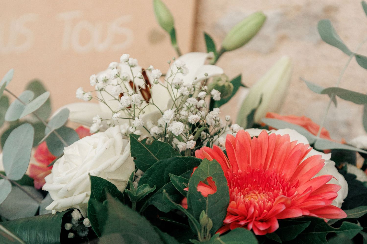 Close-up of a vibrant wedding bouquet featuring coral gerbera, white roses, and eucalyptus.