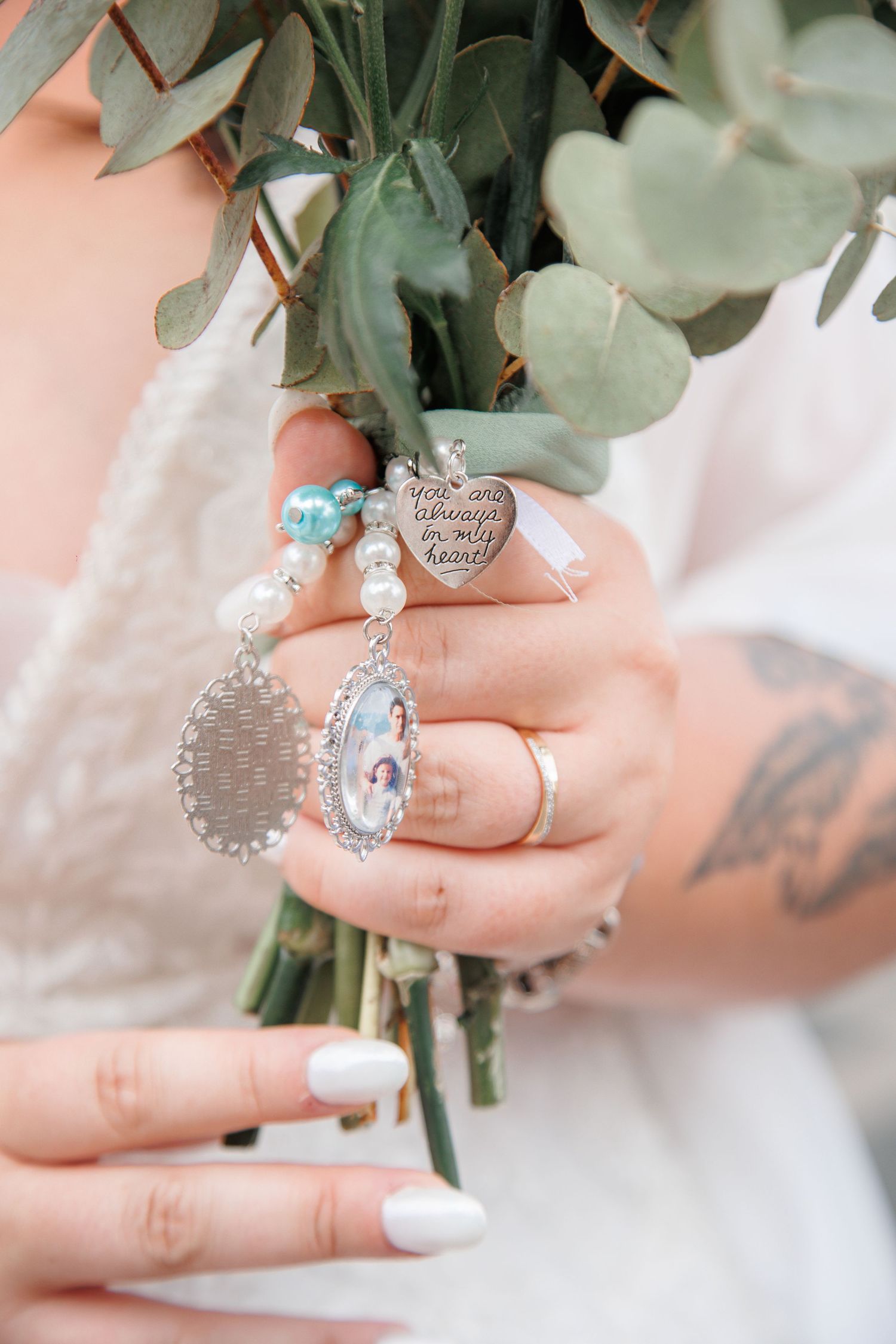 Bride holding wedding bouquet with memorial charms including heart pendant and photo locket with pearl beading.