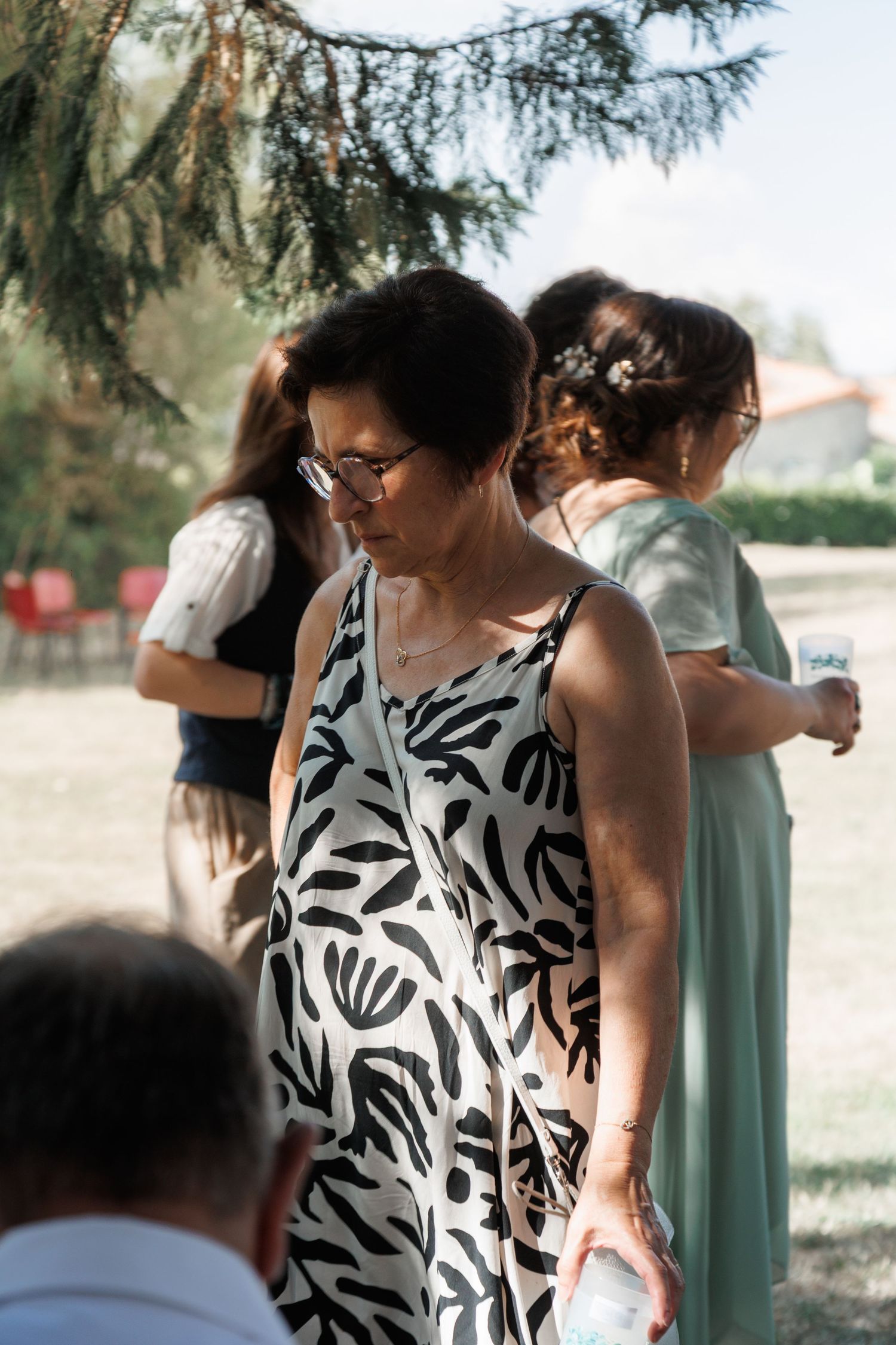 Woman in black and white floral dress at outdoor wedding gathering.