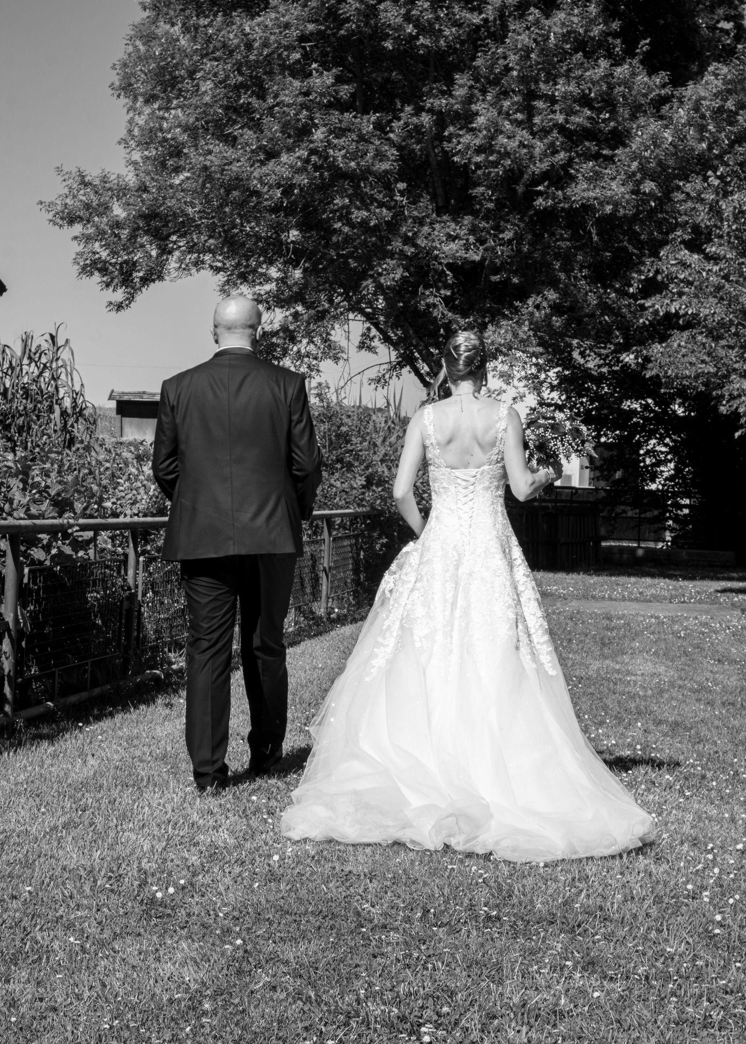 Black and white photo of bride and groom walking hand in hand through garden, bride in elegant lace ball gown.