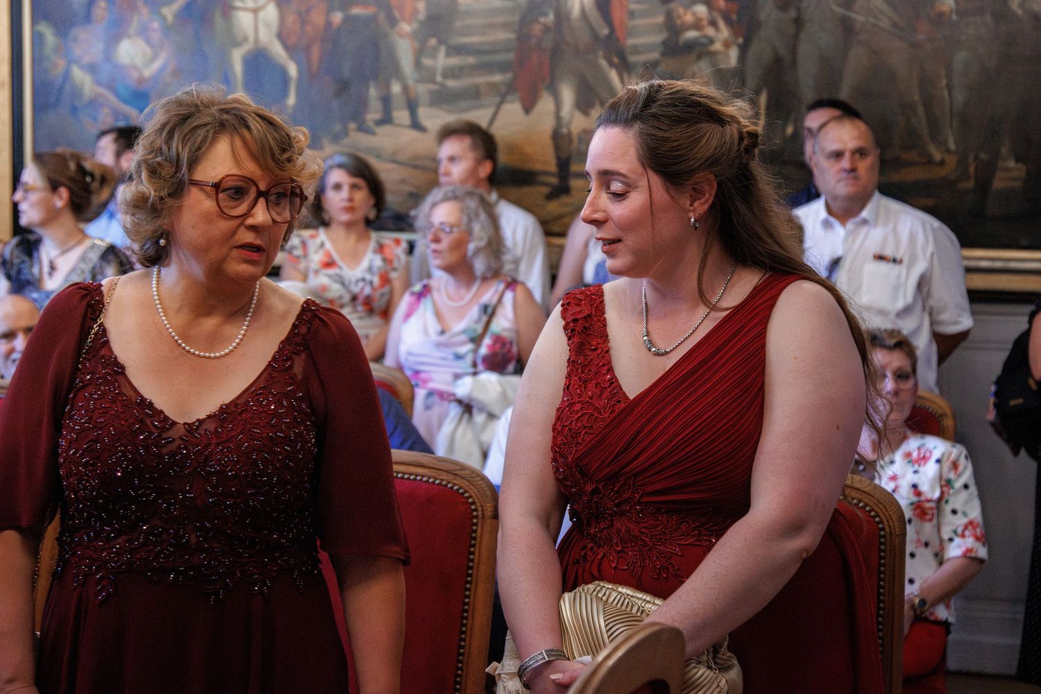 Two women in matching burgundy dresses stand together at an elegant wedding ceremony.