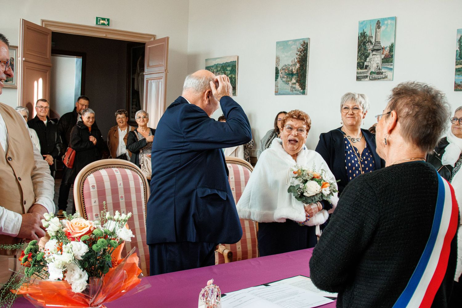 Elderly couple exchanging vows at a French civil wedding ceremony with guests and official present.