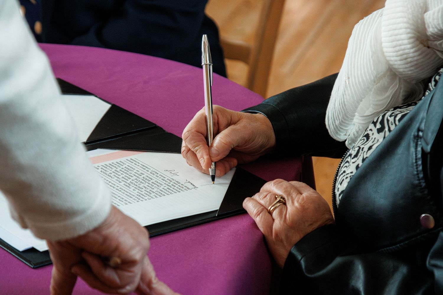 Person signing an official document with a pen at a purple table during a formal ceremony.