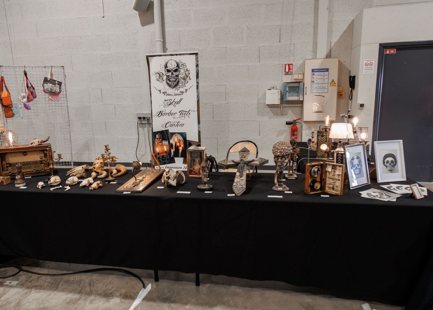 A vendor booth displaying gothic and skull-themed handcrafted items on a black draped table at an indoor convention.