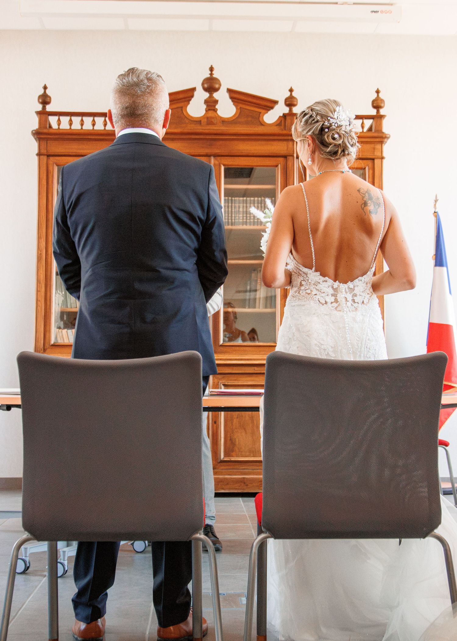 Back view of a couple standing before an ornate wooden cabinet during a ceremony.