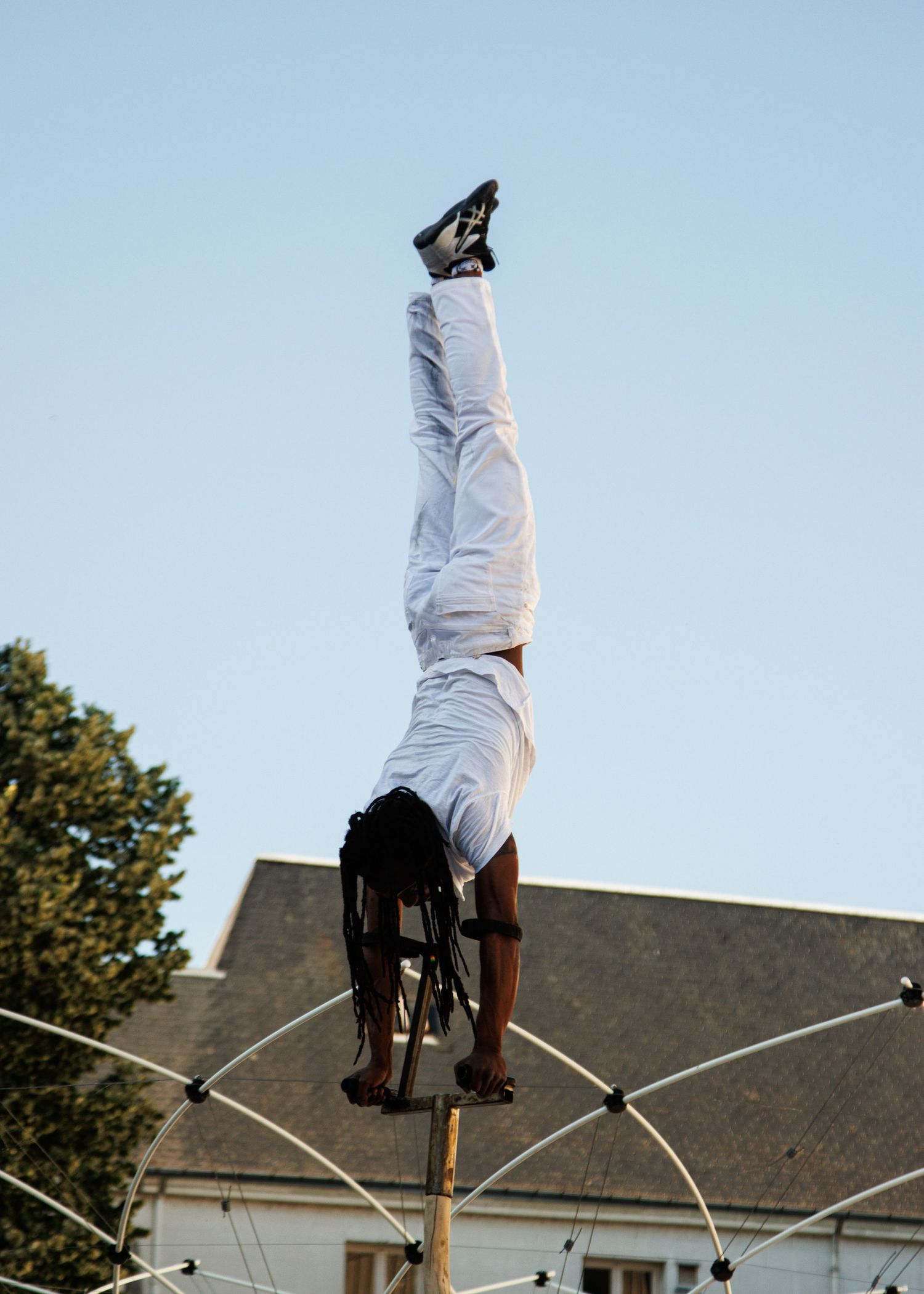 Street performer does an impressive handstand on a pole during an outdoor festival show.