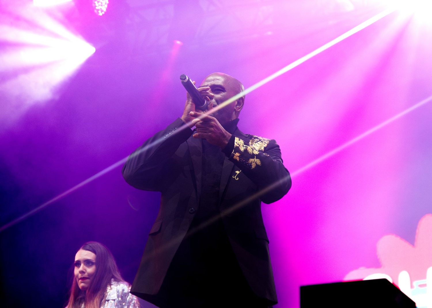 A performer in black silhouetted against vibrant pink and purple stage lighting during a concert performance.