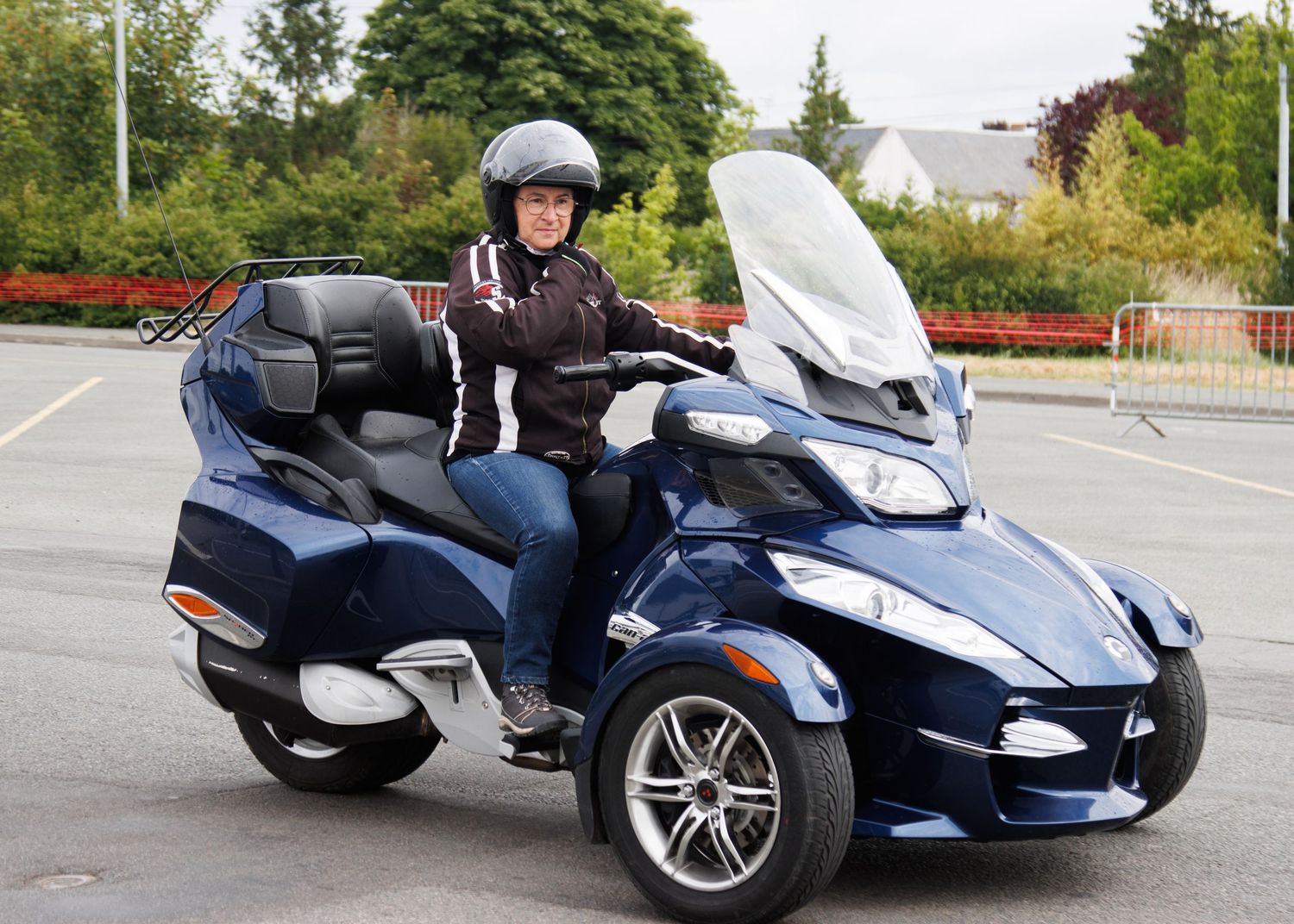 Rider on a blue Can-Am Spyder three-wheeled motorcycle in a parking lot.