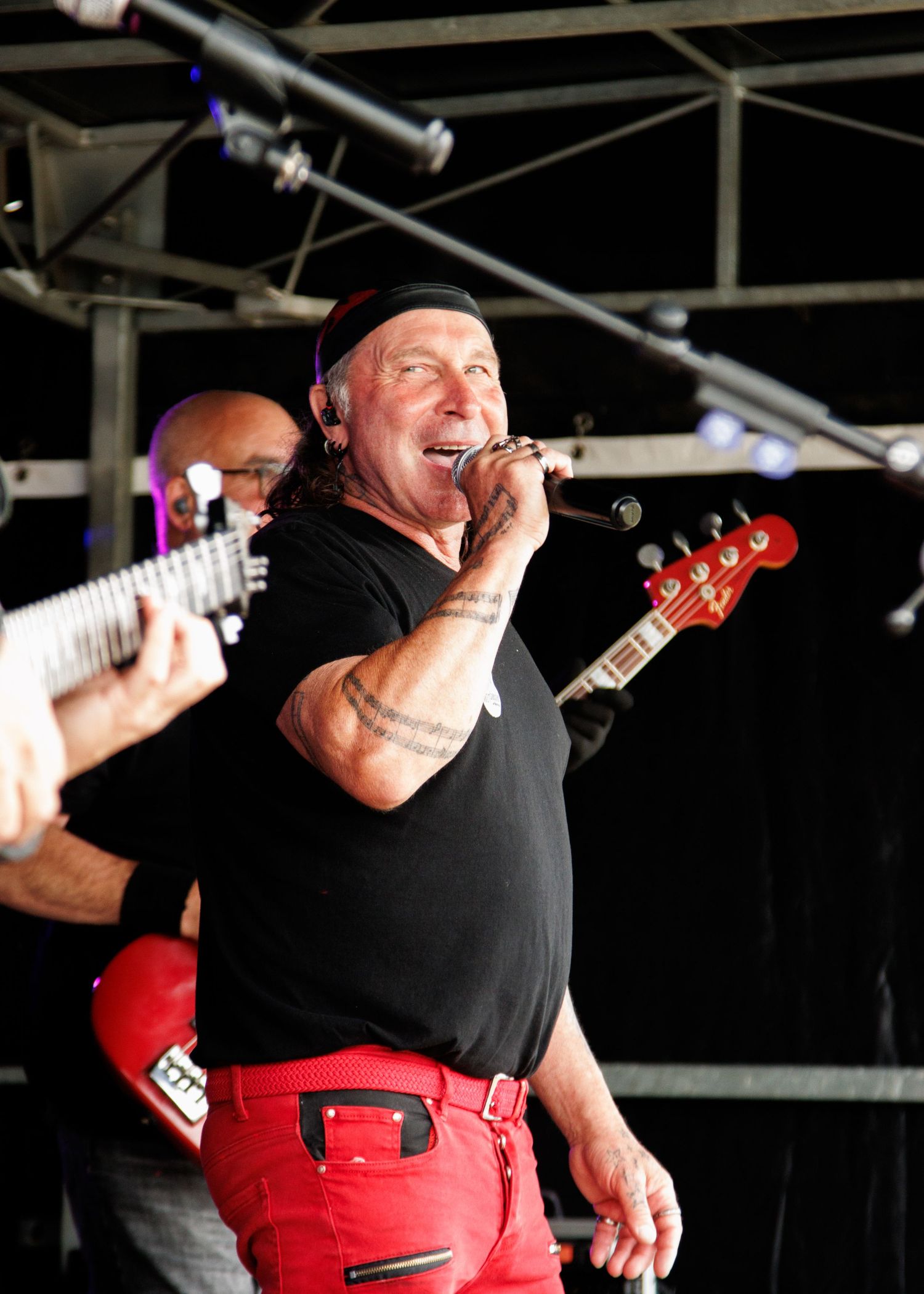 Performer in black shirt and red pants singing passionately on stage during live concert.