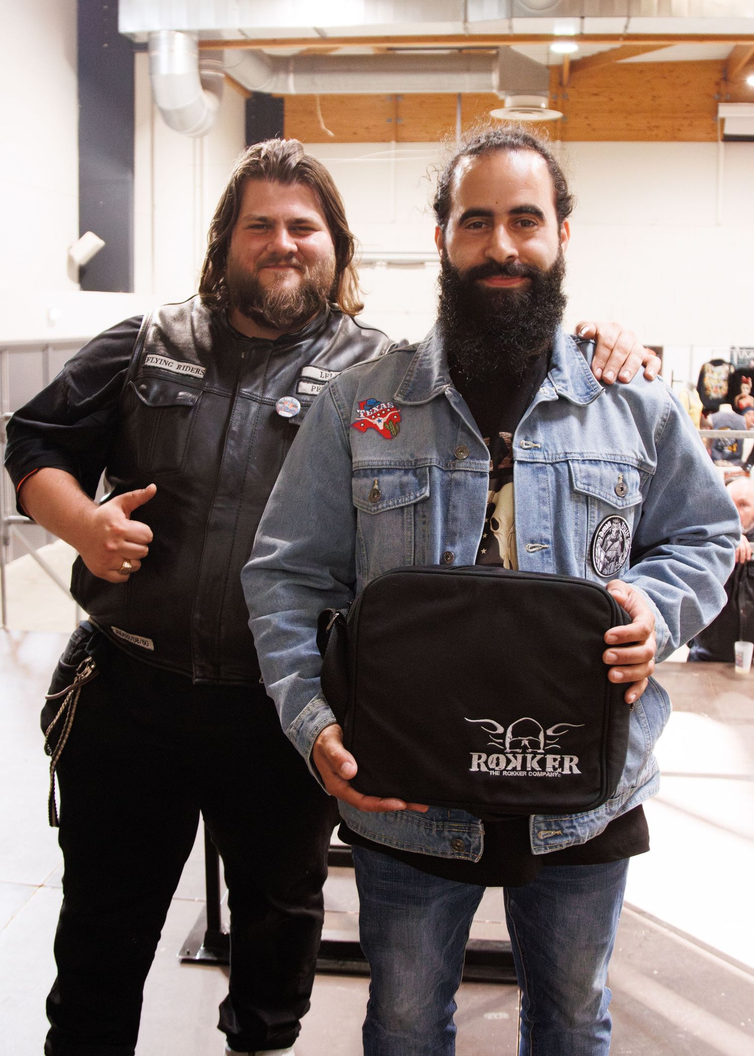 Two people in motorcycle vests pose with equipment in an indoor setting.