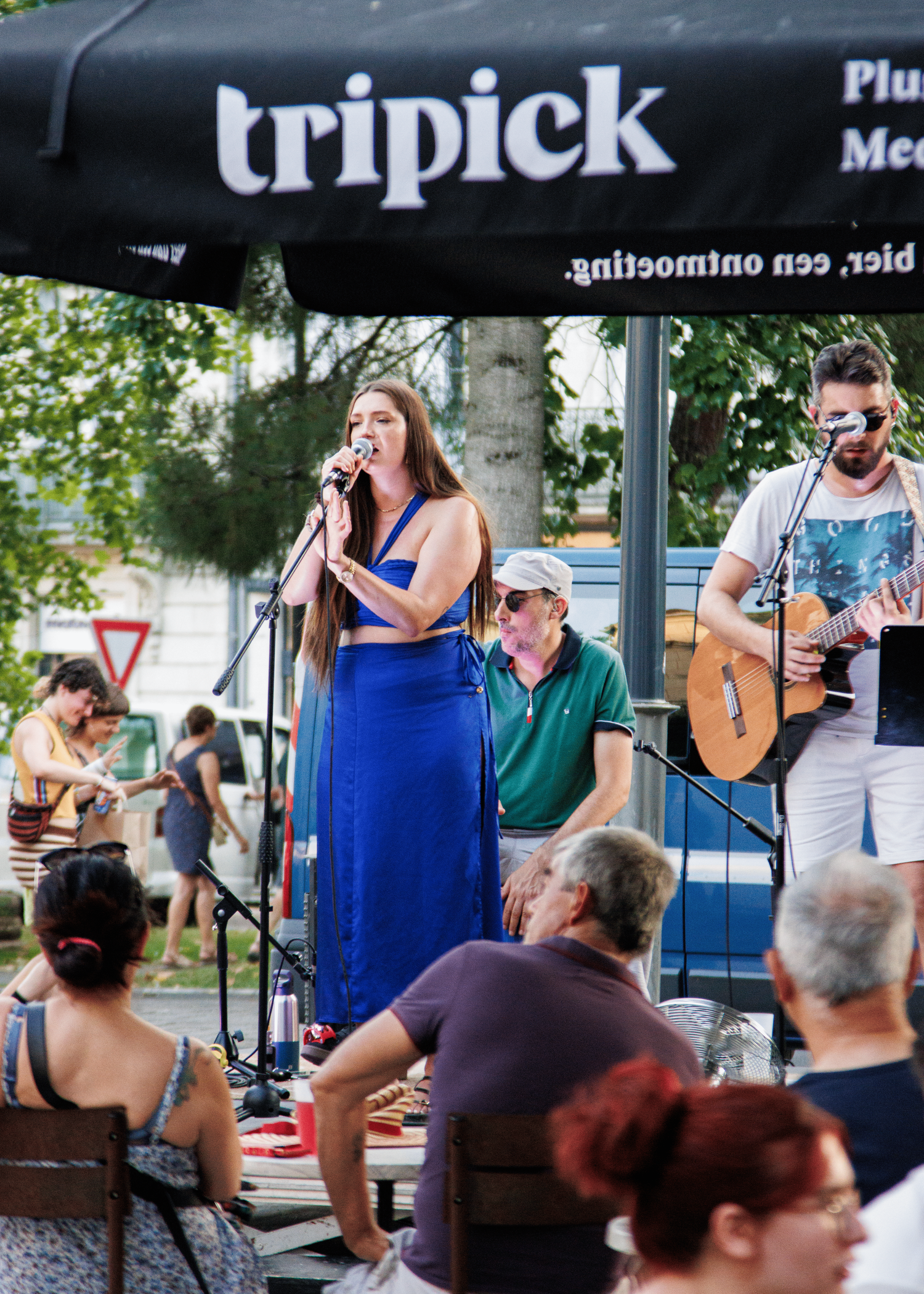 Concert audience enjoying live music at an outdoor venue with performers on stage in blue lighting.