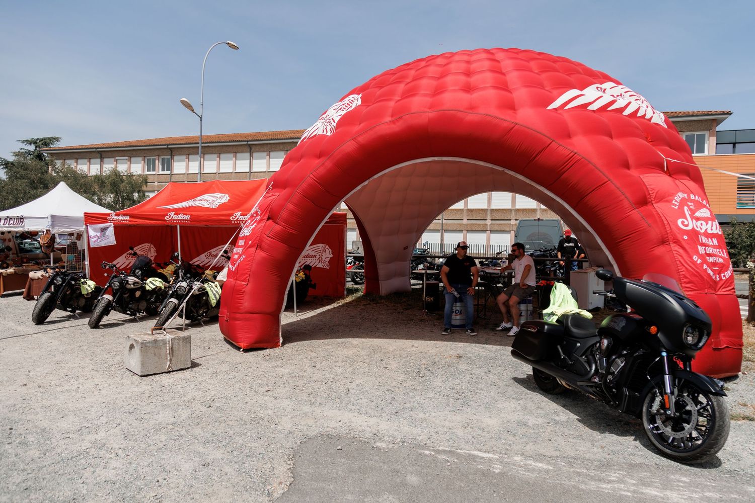 Red inflatable arch tent at an outdoor motorcycle event with Harley-Davidson bikes parked nearby on a sunny day.
