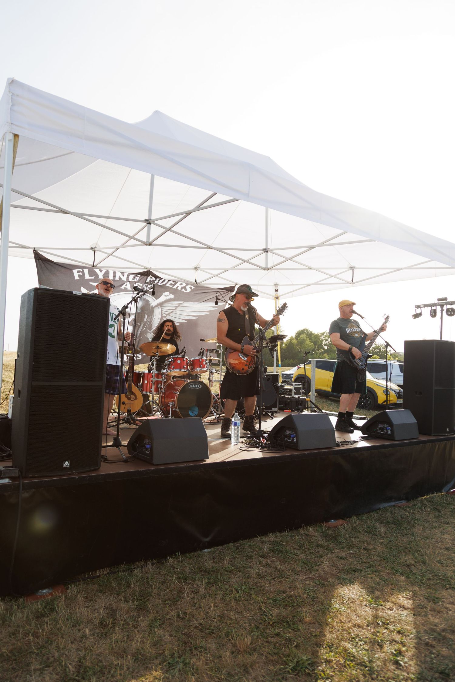 Flying Pucks band performs live on outdoor stage under white canopy tent with guitars and drums at daytime event.