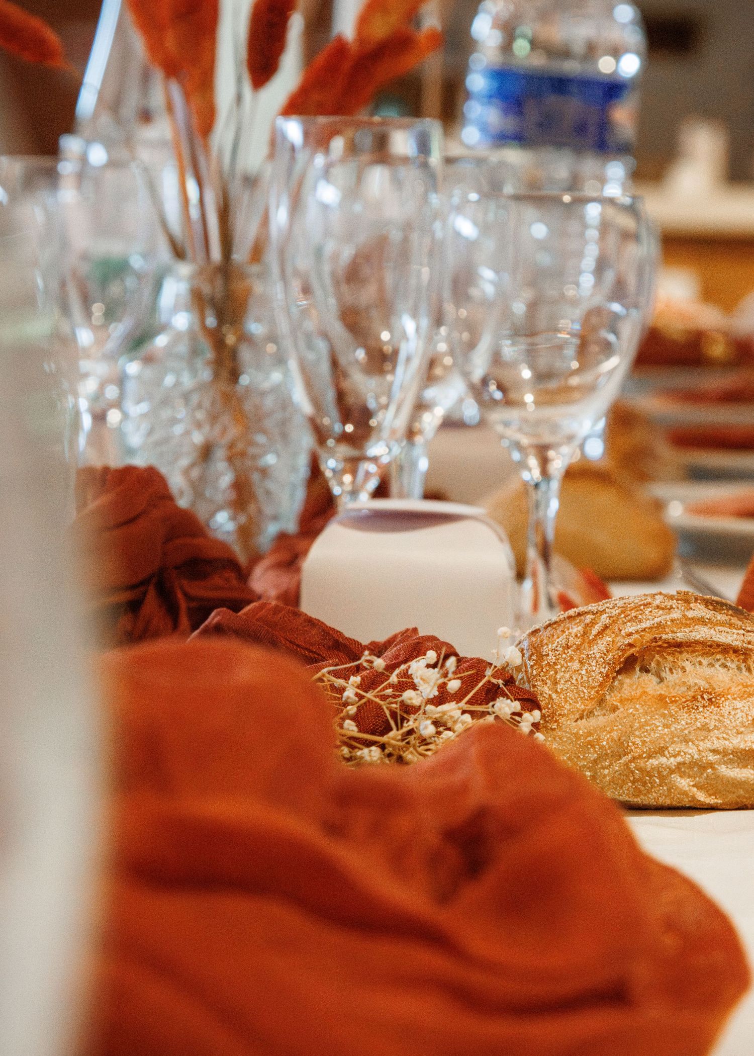 Elegant table setting with crystal wine glasses, rustic bread, and burnt orange linen on a festive dining table.