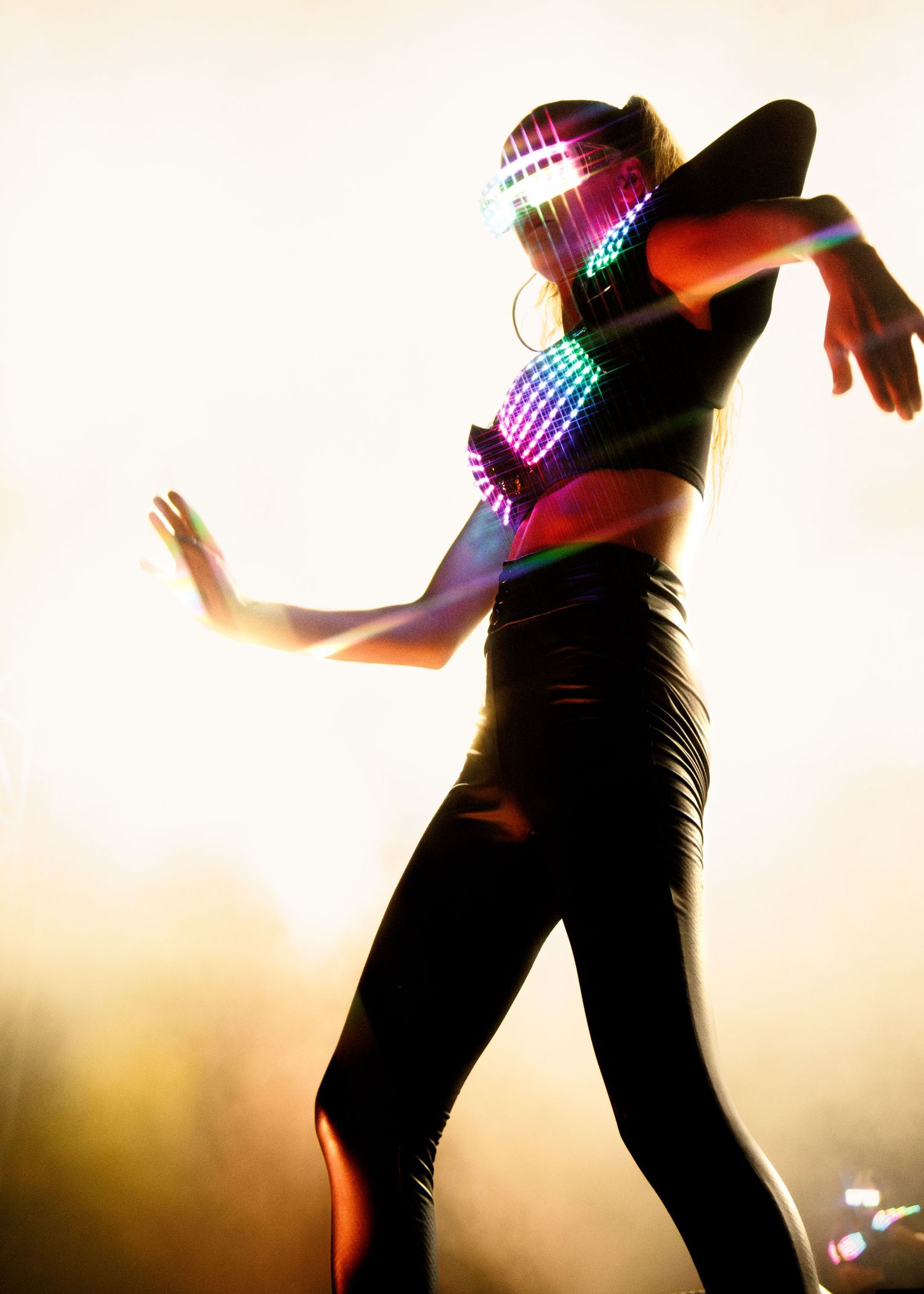 Silhouette of a dancer in black outfit striking a dramatic pose against warm backlit background with colorful lighting effects.