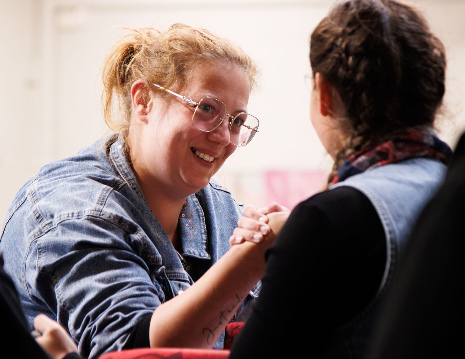 Two people engaged in friendly arm wrestling competition indoors.