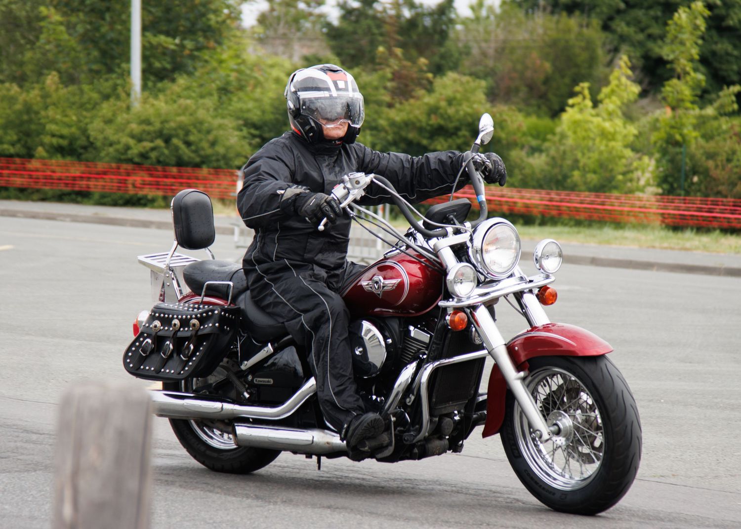 Motorcyclist riding a classic red cruiser bike with saddlebags on scenic road.