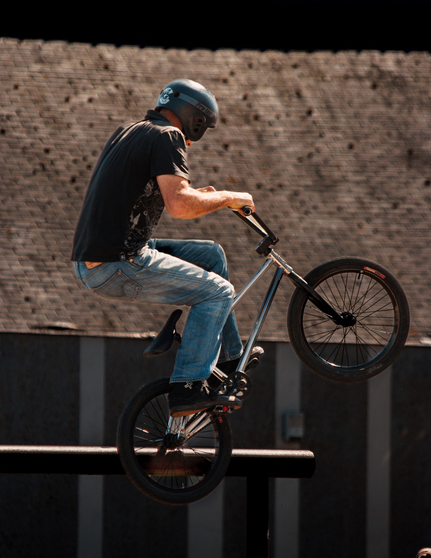 BMX rider silhouetted against brick wall performs aerial trick at dusk.
