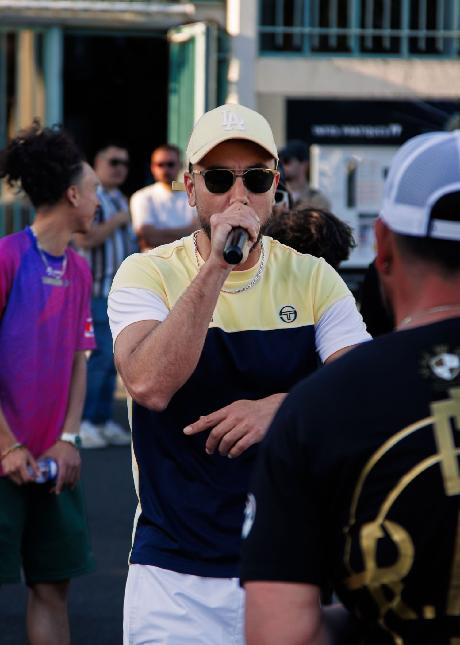 Performer in yellow and navy shirt with cap performs at outdoor venue.