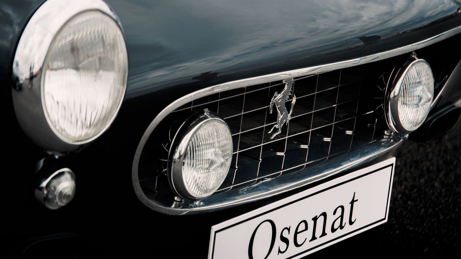 Classic car front grille and headlight detail with Osena badge.