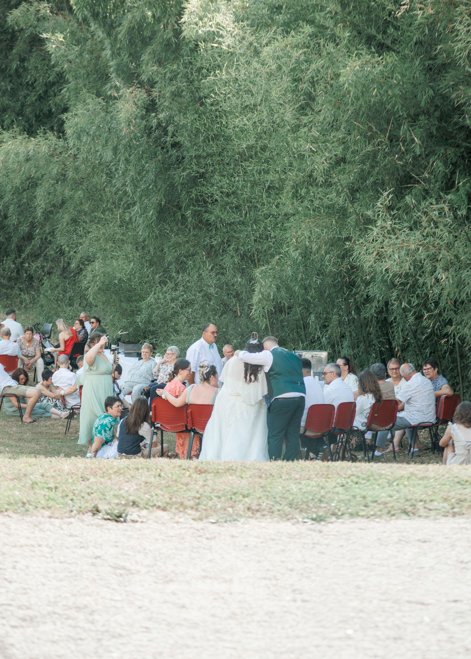 Wedding guests seated outdoors near weeping willow trees during an outdoor ceremony.