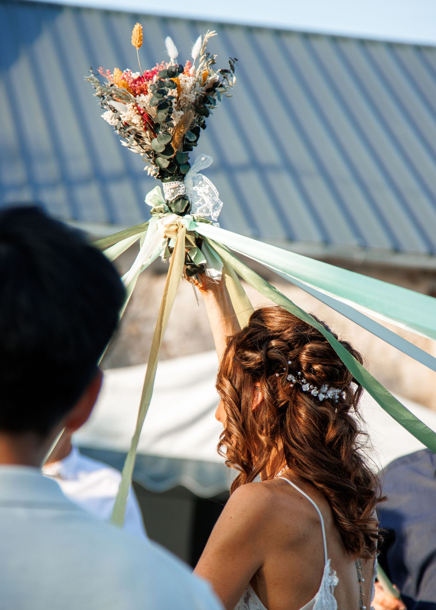 Outdoor wedding celebration with a white parasol and floral arrangements against a blue building backdrop.