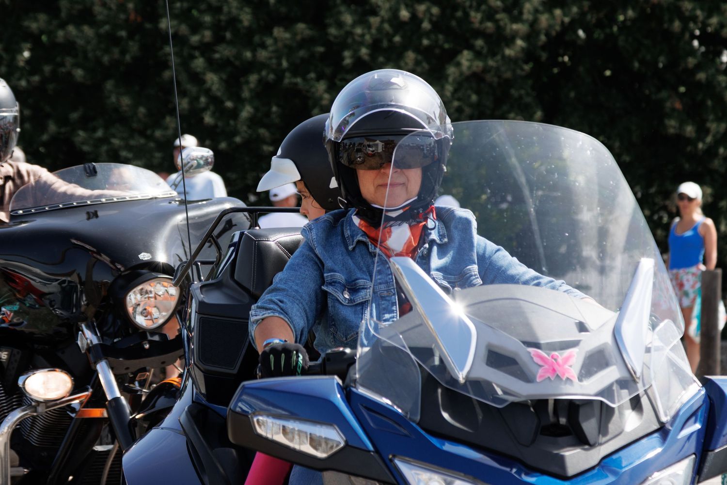 Child wearing helmet riding a motorcycle at an outdoor biker event on a sunny day.