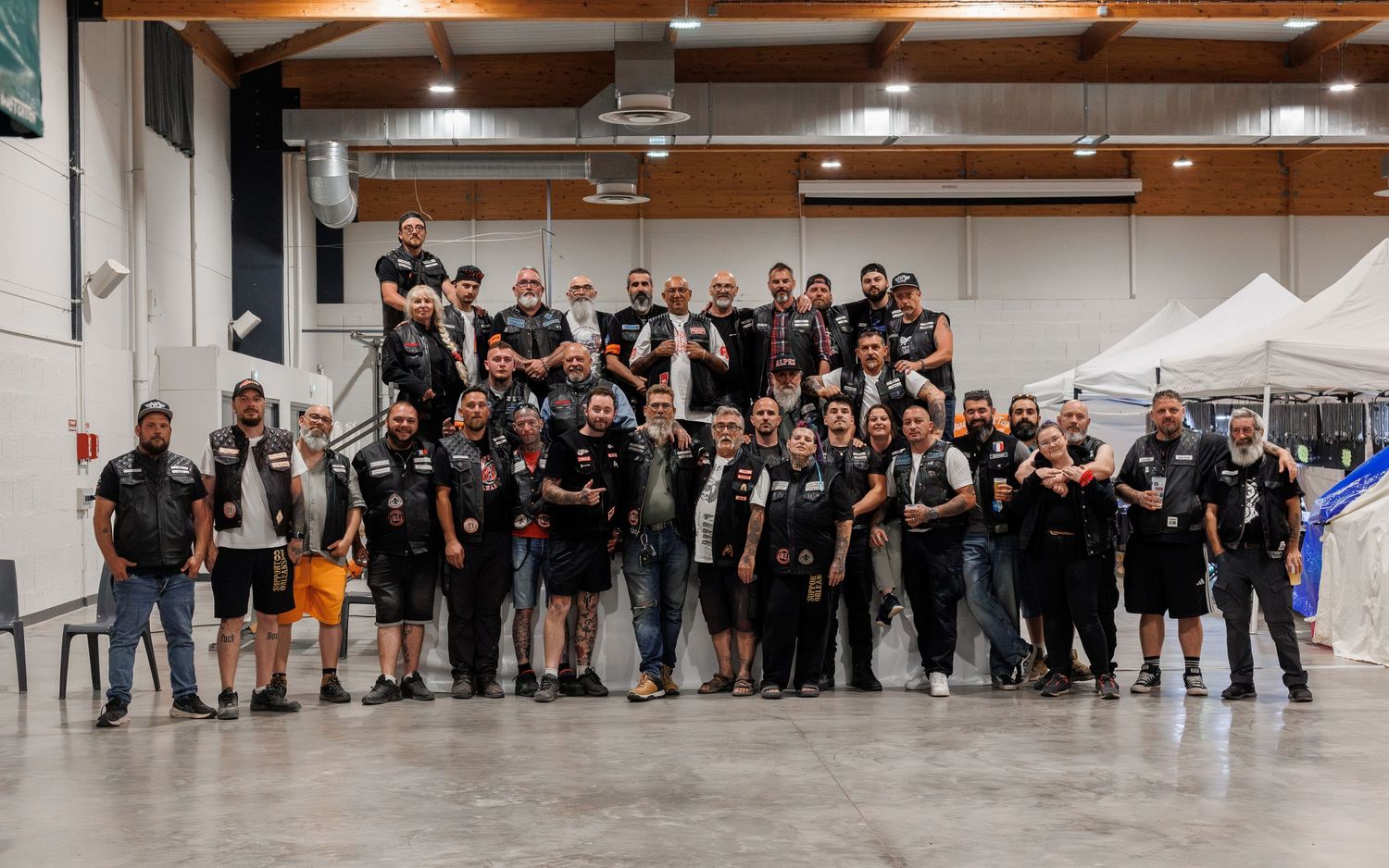 Large group of motorcycle club members in matching jackets posing together inside an event venue.
