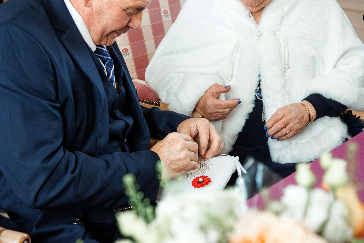 Elderly couple exchanging rings at a wedding ceremony, with flowers in the foreground.