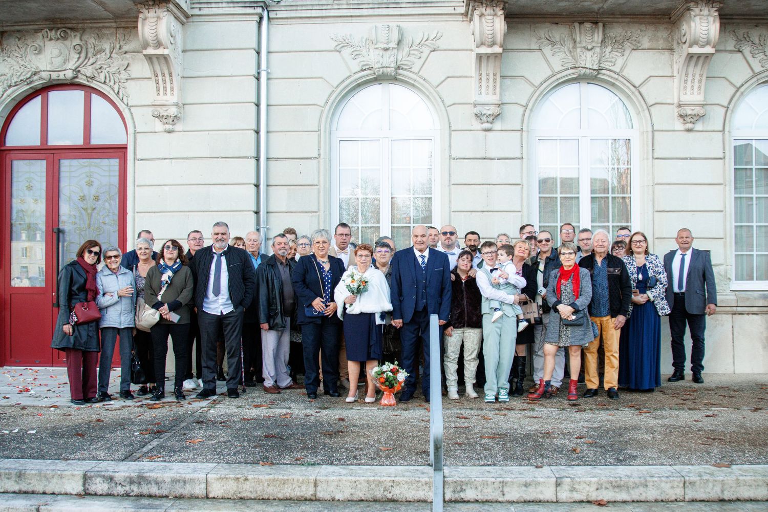 Large group of people posing for a formal photo outside a historic European building with red doors.