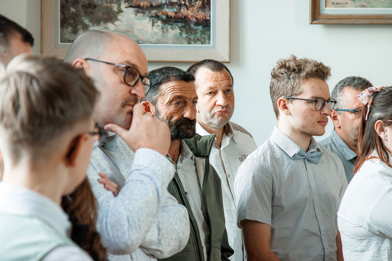 Group of men engaged in conversation at an indoor art gallery event with paintings on the wall.
