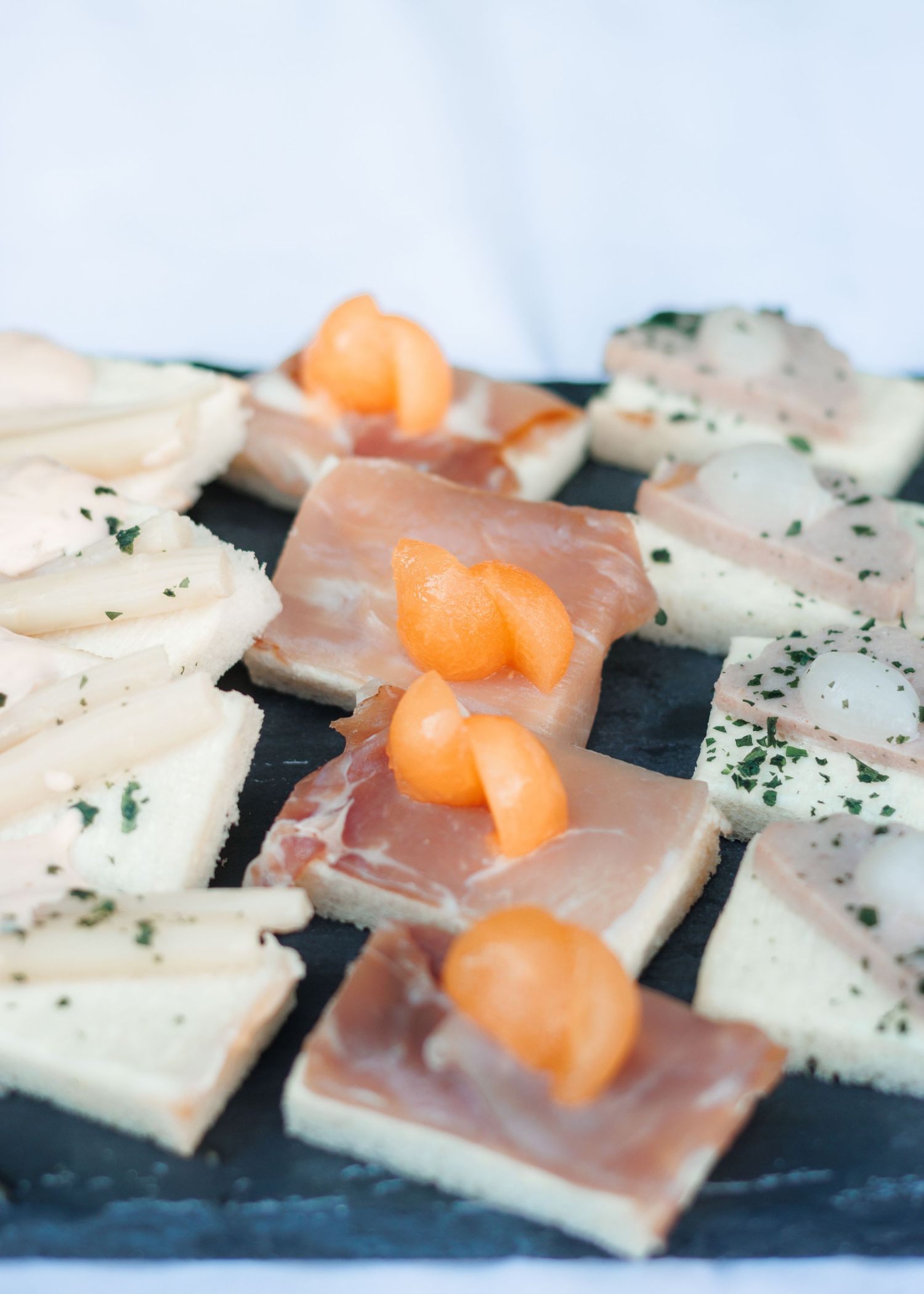 Elegant wedding appetizers on slate board featuring prosciutto, cheese slices, and melon garnish.