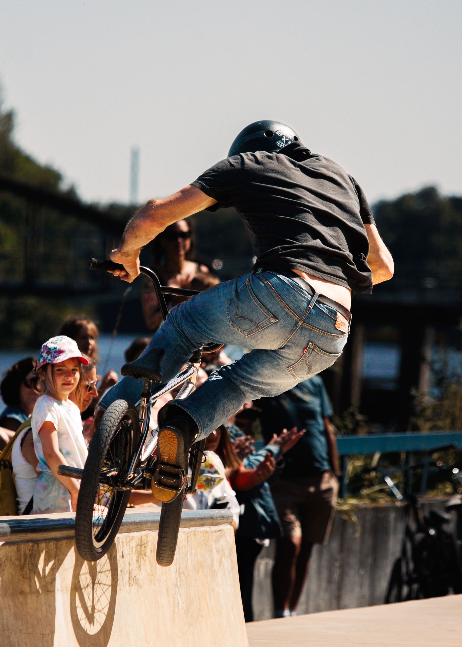 BMX rider performing stunt jump off concrete ledge with crowd watching in background.