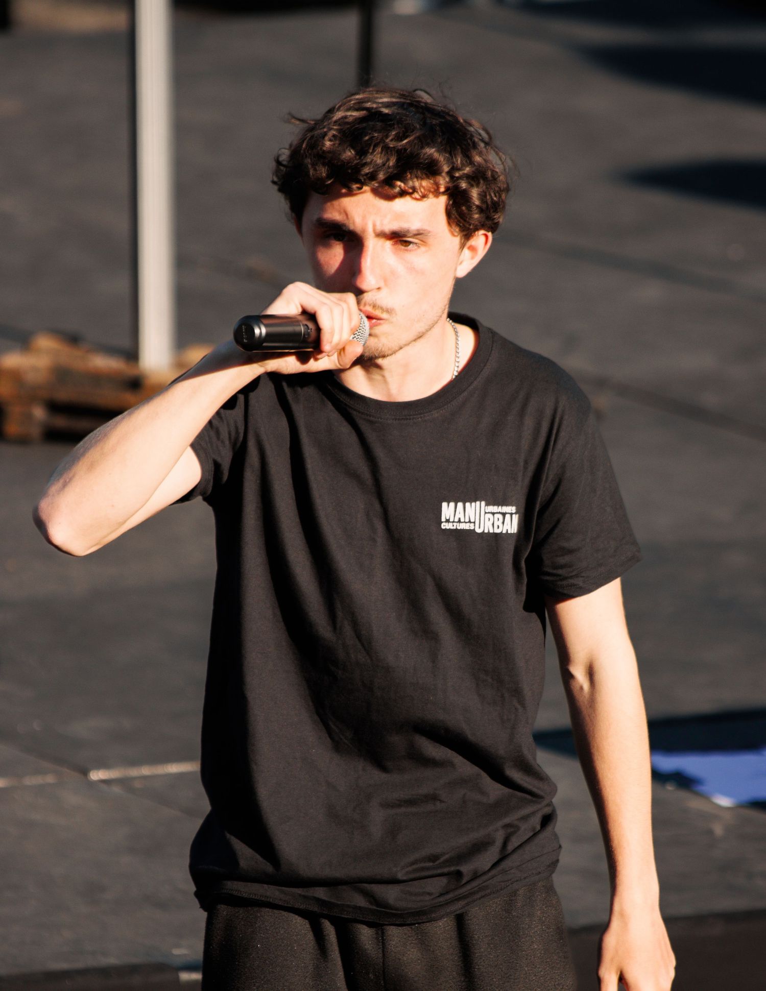 Performer in black t-shirt holds microphone during outdoor show.