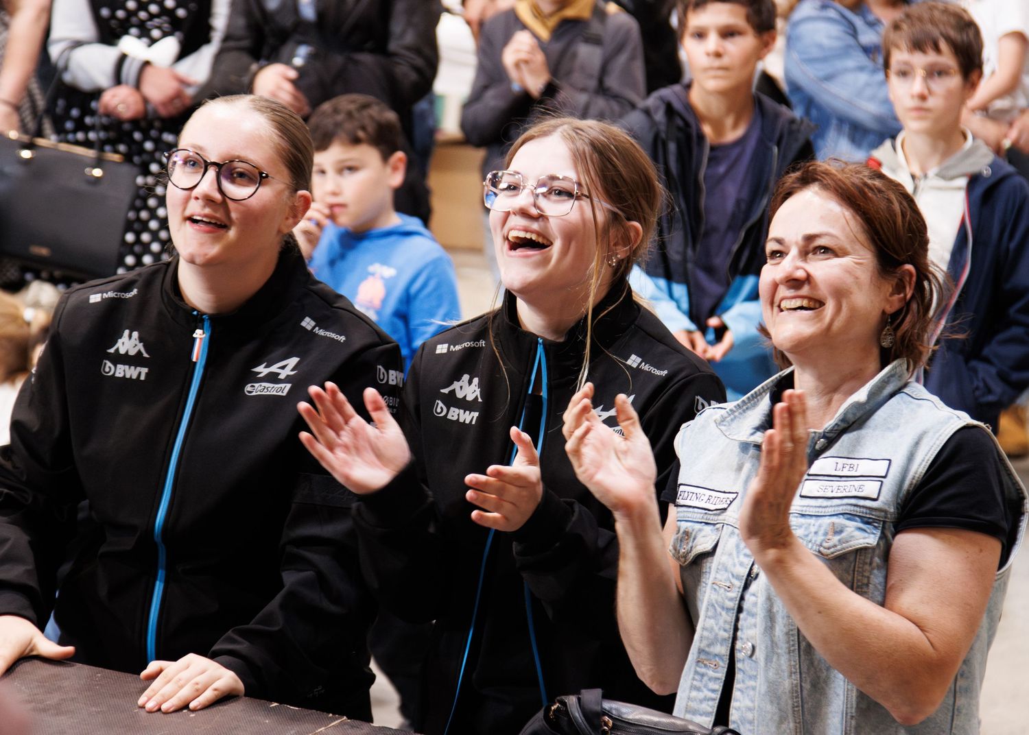 Three enthusiastic spectators cheering and clapping while watching an event.