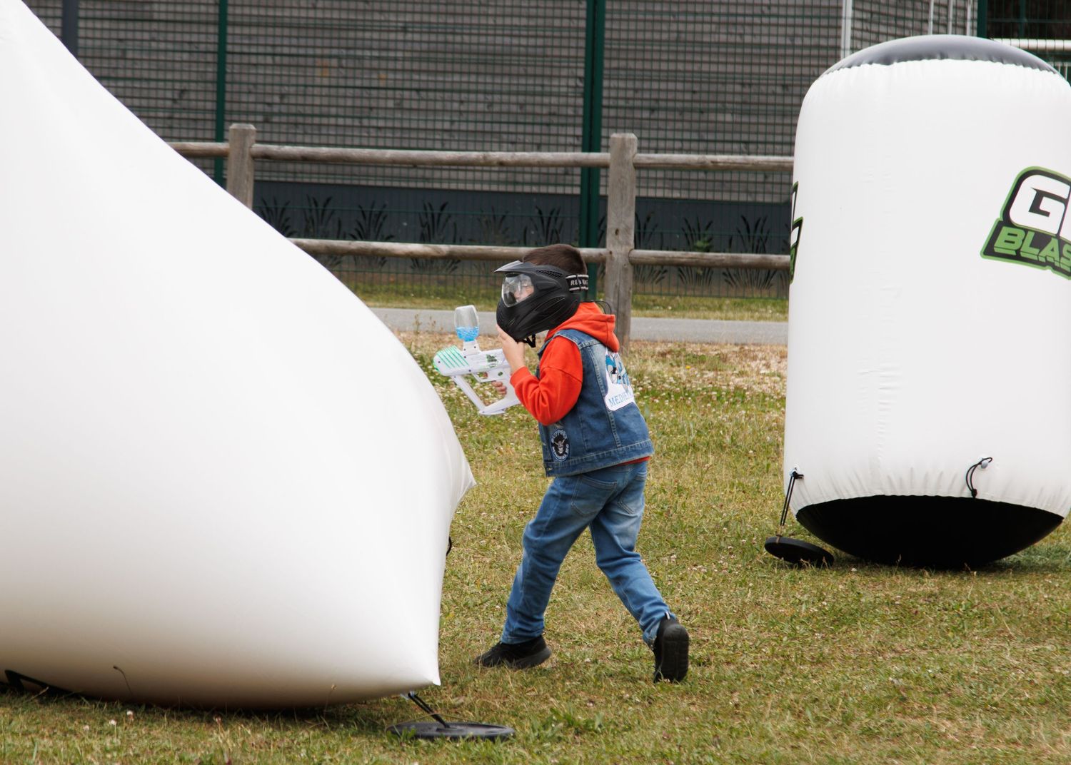 Child in overalls plays behind inflatable white barriers during outdoor game.