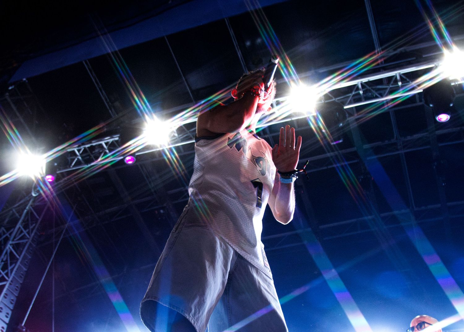 A performer in white clothing sings on stage under dramatic blue lighting and bright spotlights during a live concert.