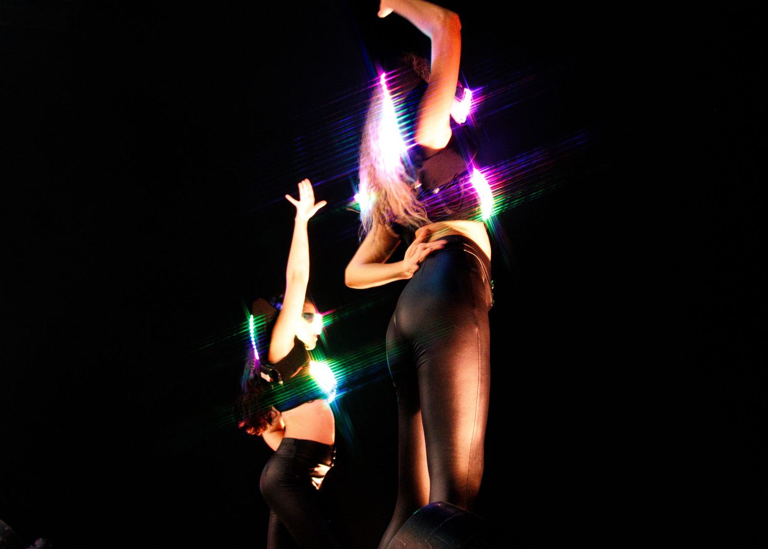 Performers in dramatic black silhouettes create a captivating display of multicolored light effects during dark performance.