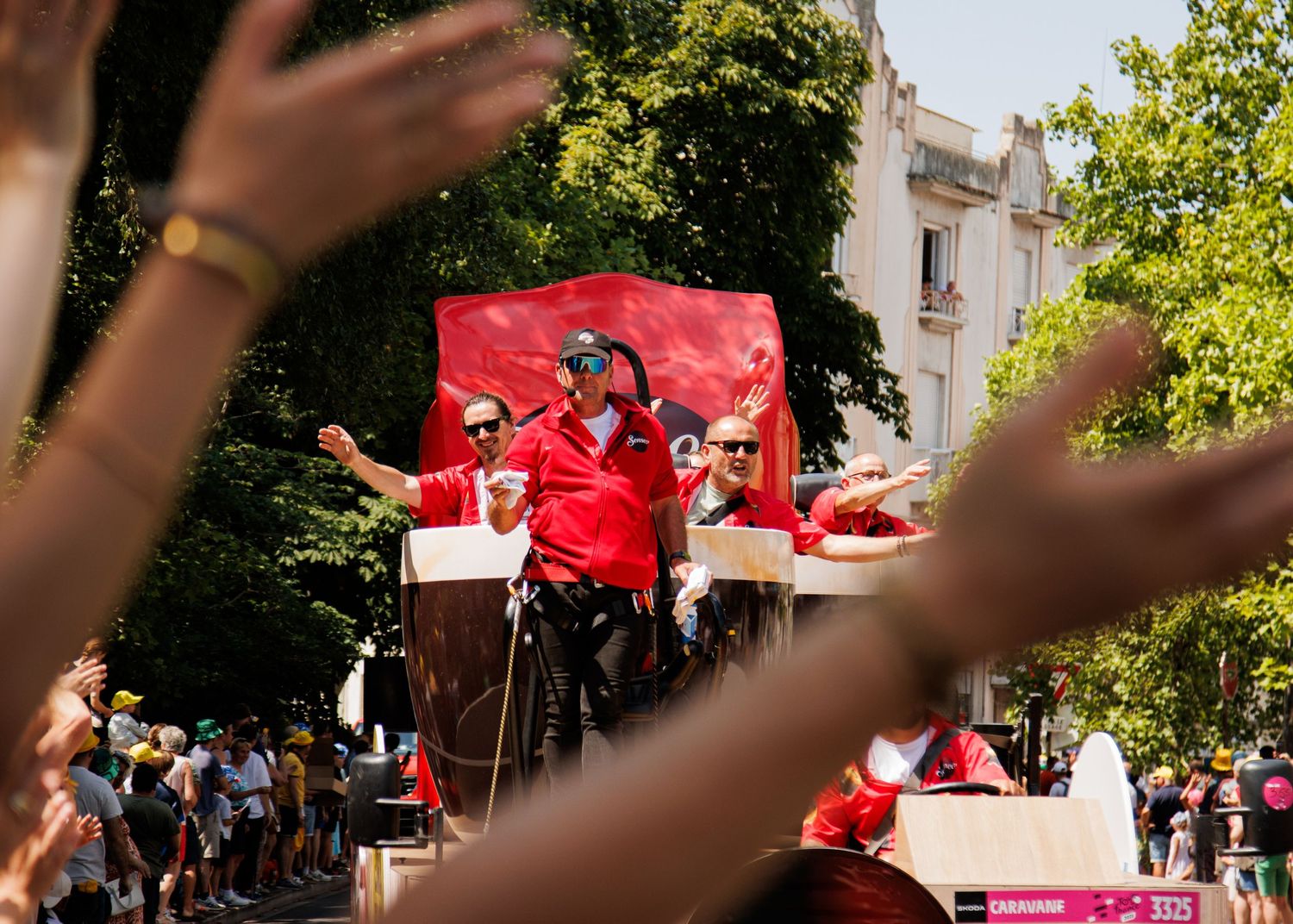 Crowd cheers as performers on a red float engage with spectators during a street parade.