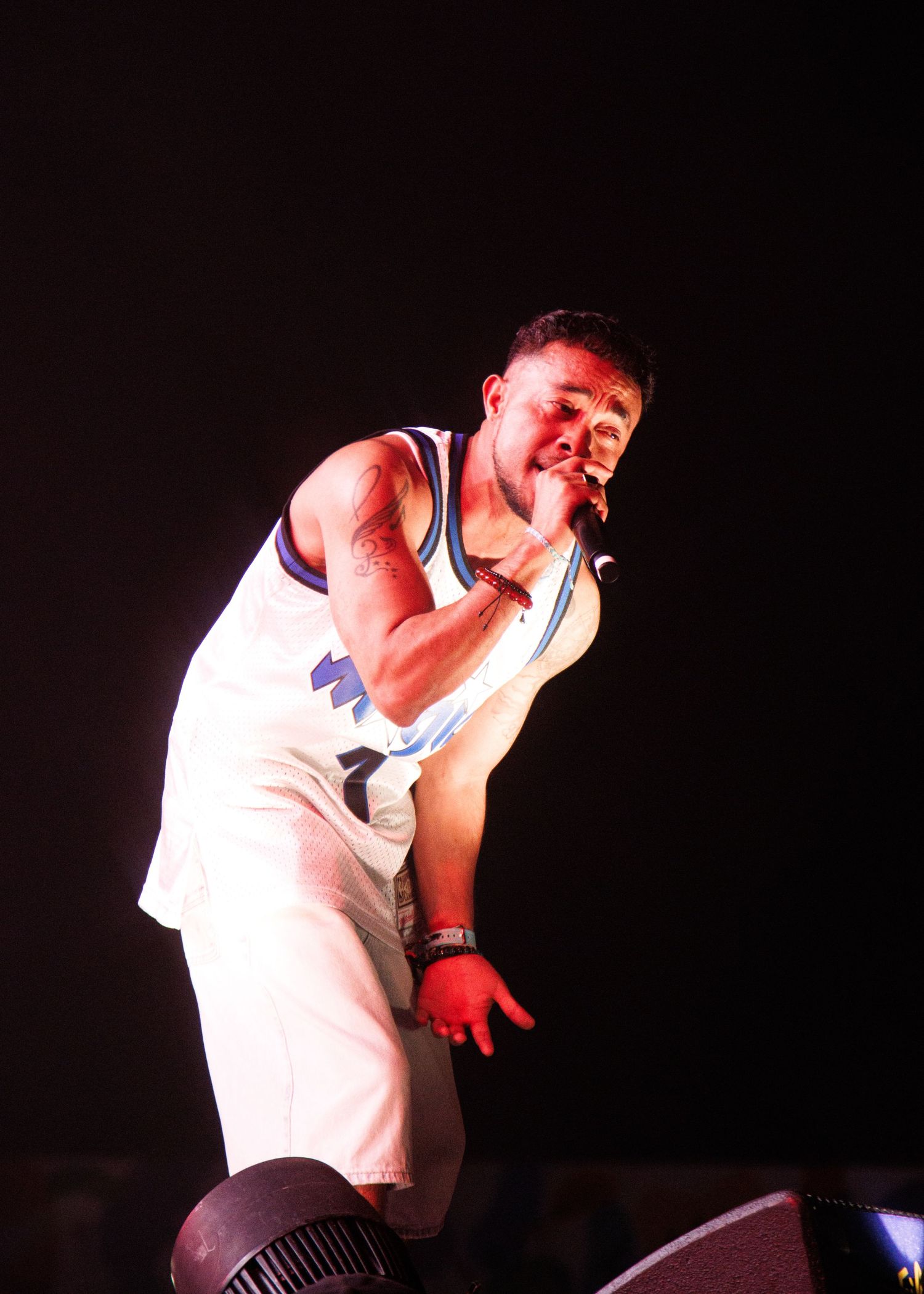 Singer wearing a white sleeveless top performs energetically in a series of dramatic stage poses on a dark background.
