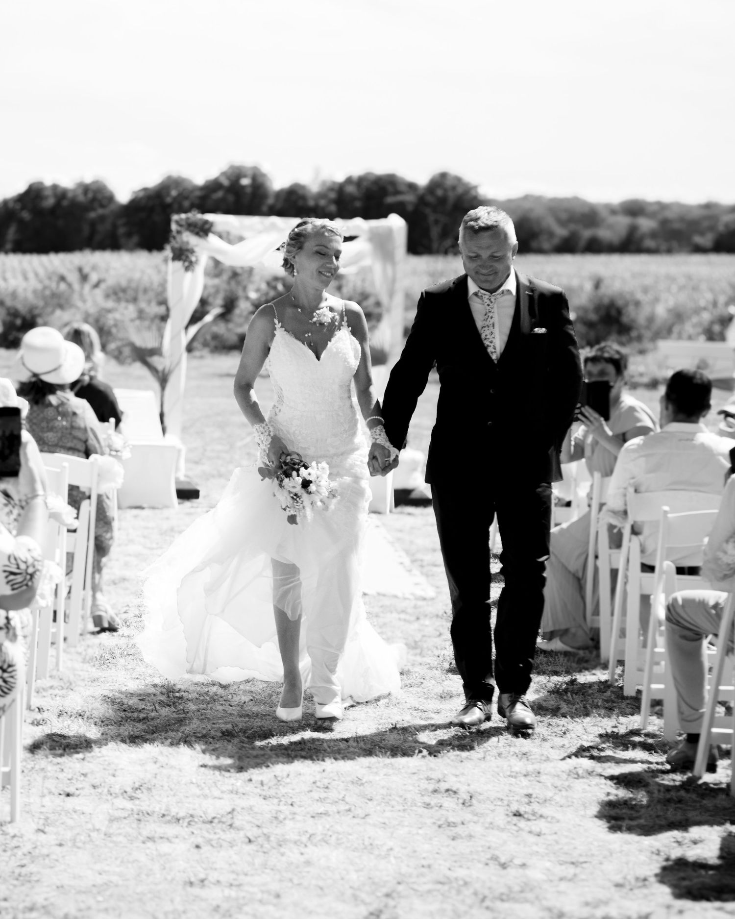 A black and white photo of a couple walking down the aisle after their outdoor wedding ceremony.