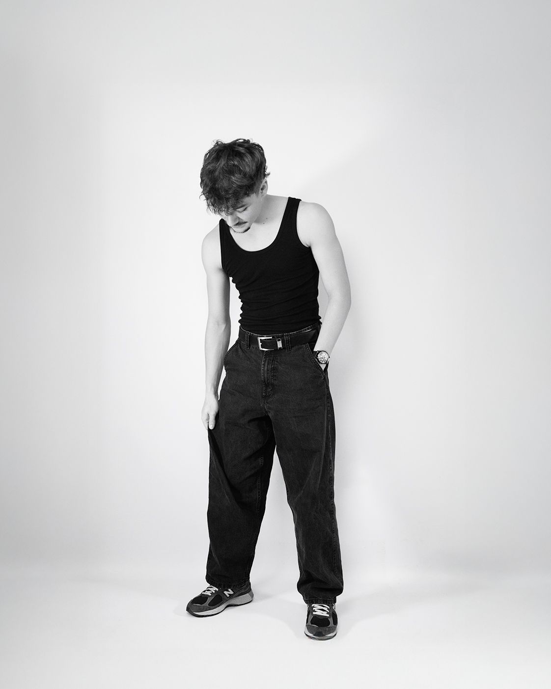 A person wearing black overalls and tank top poses in different positions against a white studio backdrop.