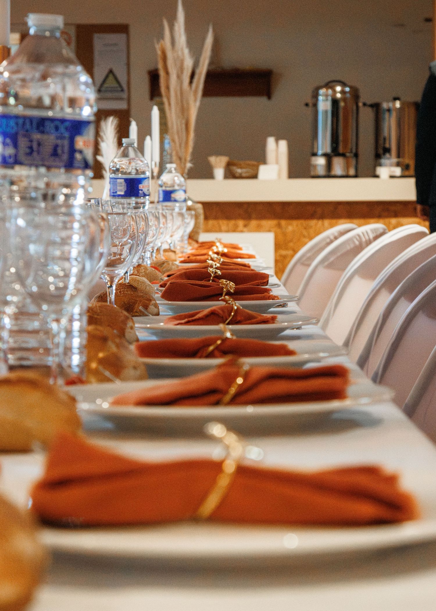Elegant long dining table set with orange napkins, crystal glasses, and water bottles for a formal event.