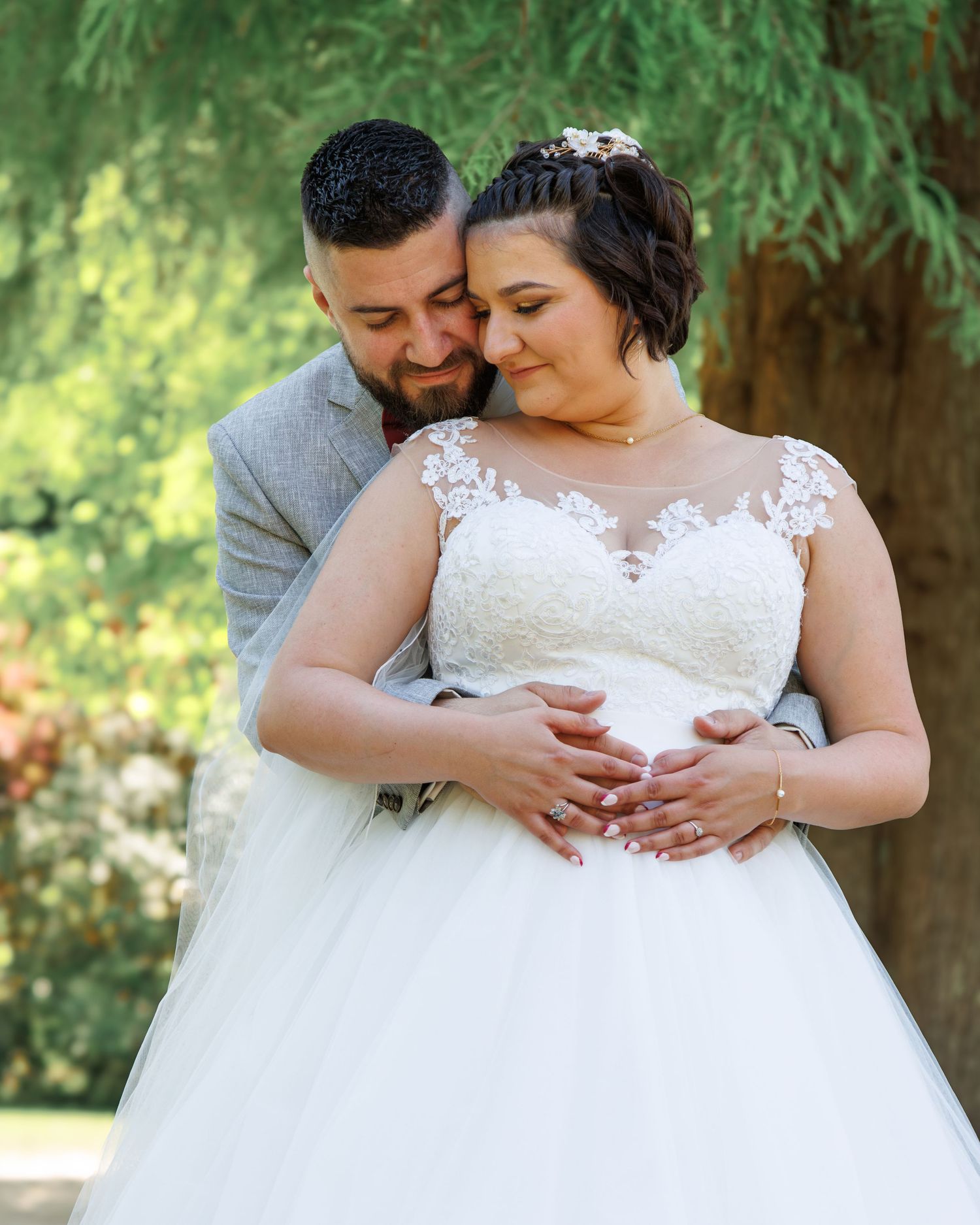Intimate outdoor wedding portrait showing tender embrace under green trees.